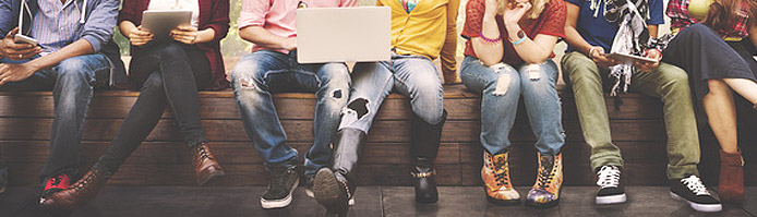 Freunde die auf einer Bank sitzen und mit ihren mobilen Geräten auf Facebook surfen